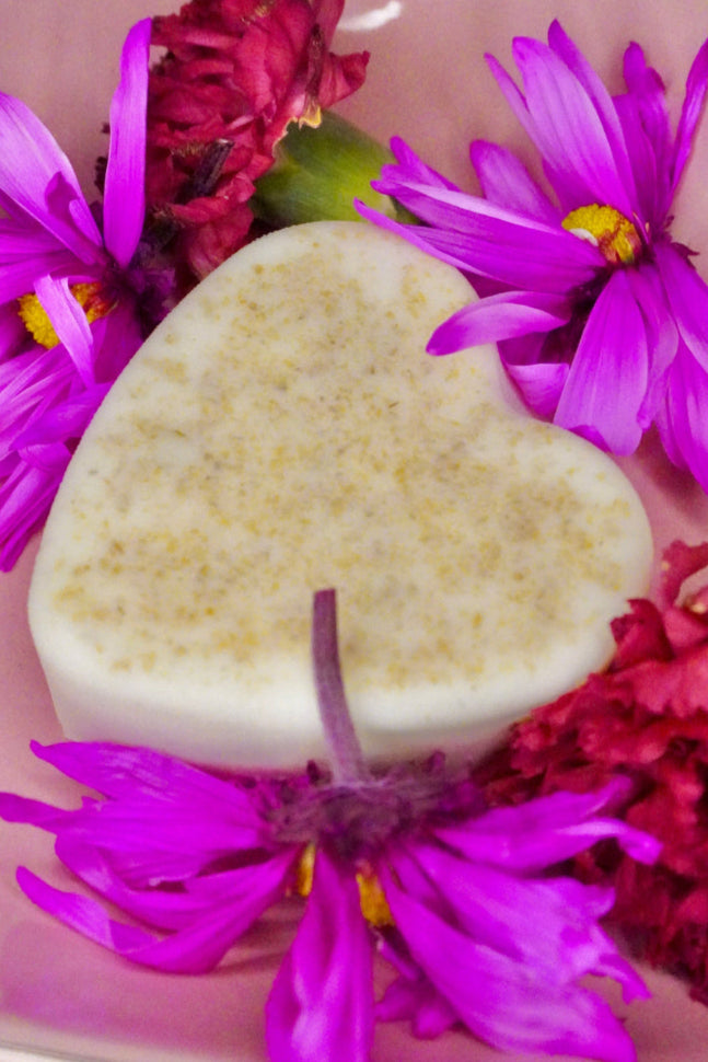 Heart-shaped bar of soap surrounded by pink and purple flowers on a pink background